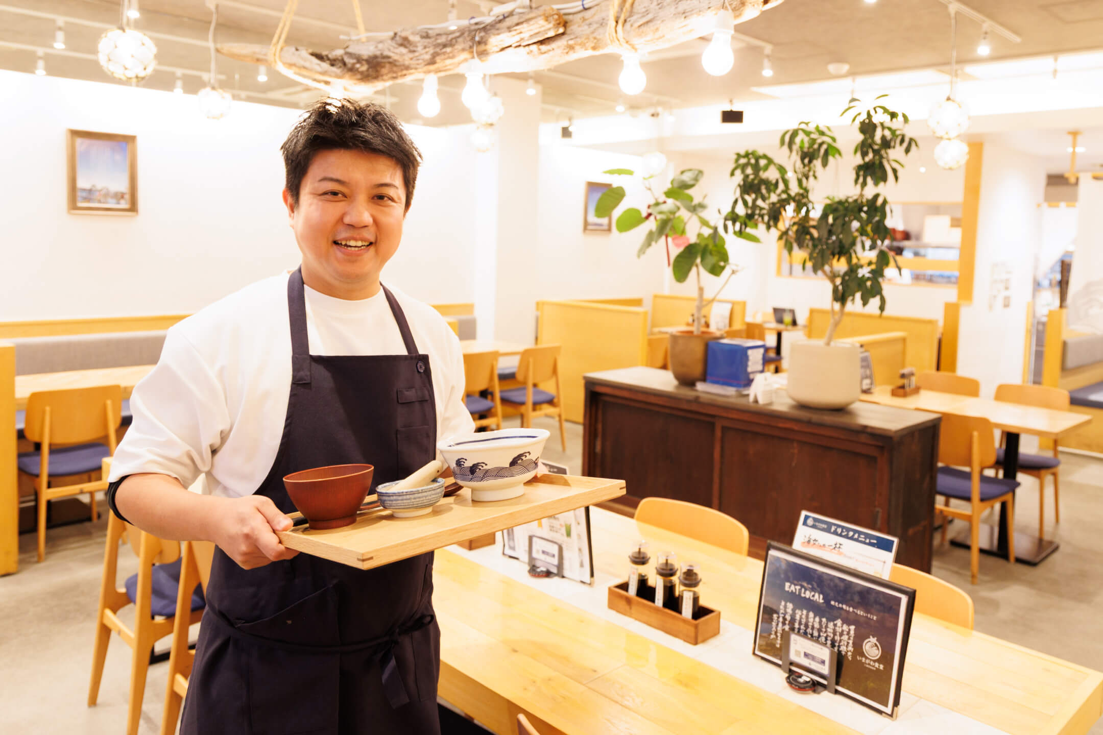 定食が乗ったトレーを手に、柔らかな表情でこちらに視線を向ける様子